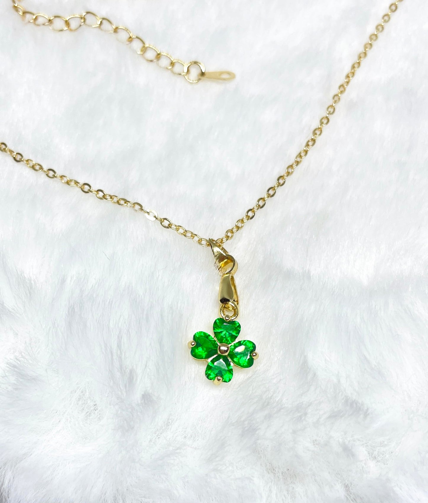A gold necklace with a green four-leaf clover pendant.