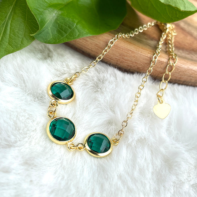 A gold chain necklace with emerald green gemstones.