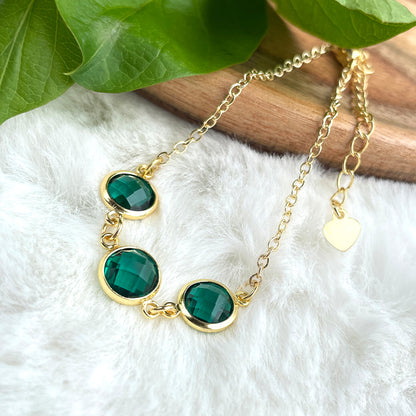 A gold chain necklace with emerald green gemstones.